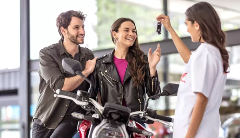 vendedora da concessionaria honda entregando nas maos de um casal de homem e mulher as chaves da sua moto honda - Moto Honda Motopel