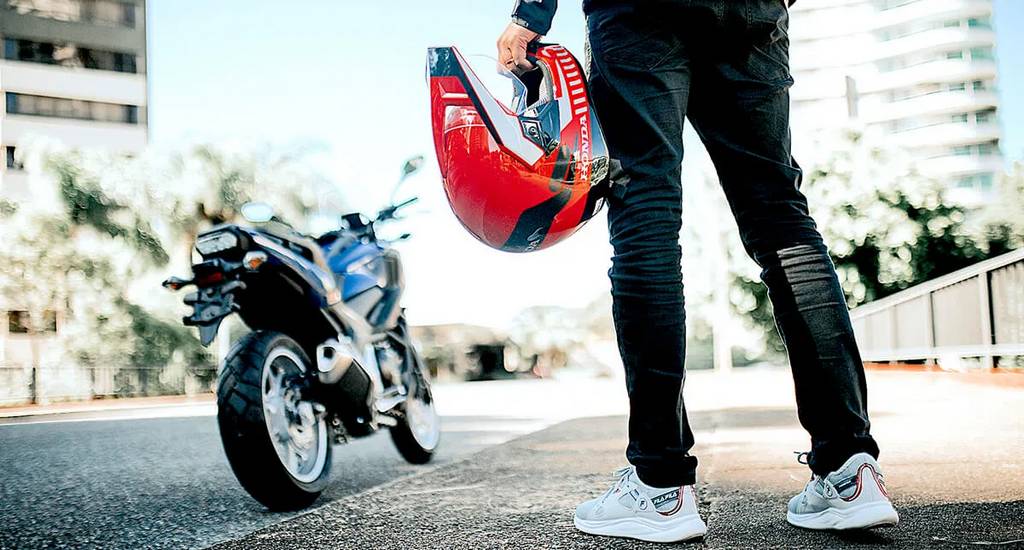 homem a frente da moto segurando seu capacete honda vermelho - Moto Honda Motopel