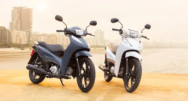 duas motocicletas honda biz 125 nas cores azul marinho e branca estacionadas na praia a beira mar - Moto Honda Motopel